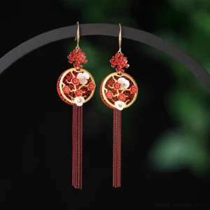 Traditional Chinese red and gold plum blossom tassel hook earrings with hollow round floral pendants, shell flower embellishments, and layered red chain tassels on a display stand