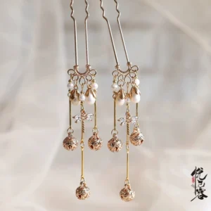 Close-up of a traditional Chinese gold-toned U-shaped hairpin with imitation pearls hollow bell pendants crystal accents and dangling tassels on soft gauze fabric