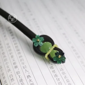Traditional Chinese wooden hair stick with dark brown shaft, green carved ornaments, jade style pendant, yellow bead details, and vintage Chinese decoration displayed on calligraphy paper