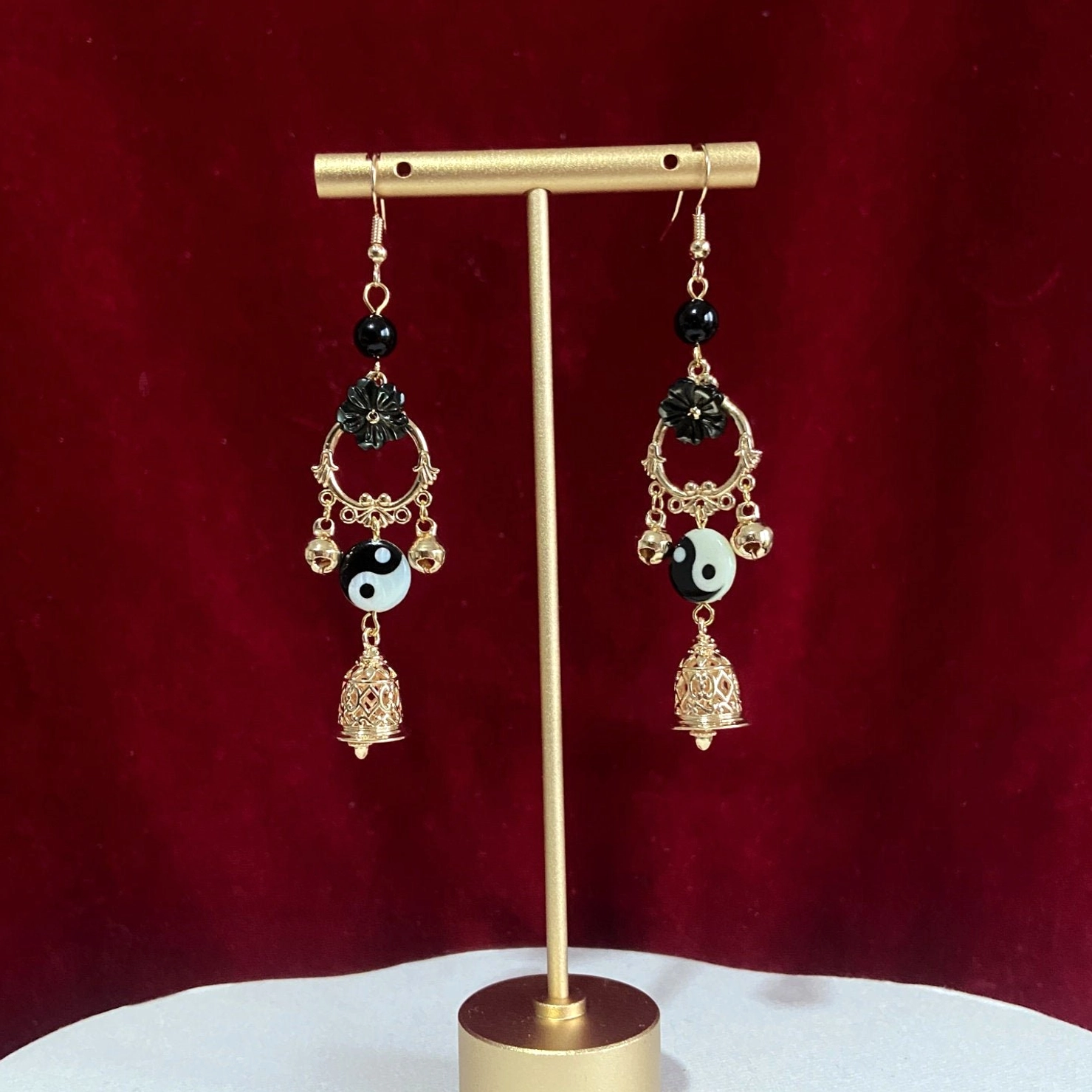 Traditional Chinese Yin Yang Hanfu dangle earrings with gold finish black floral frame Tai Chi charms and openwork bell pendants against red velvet