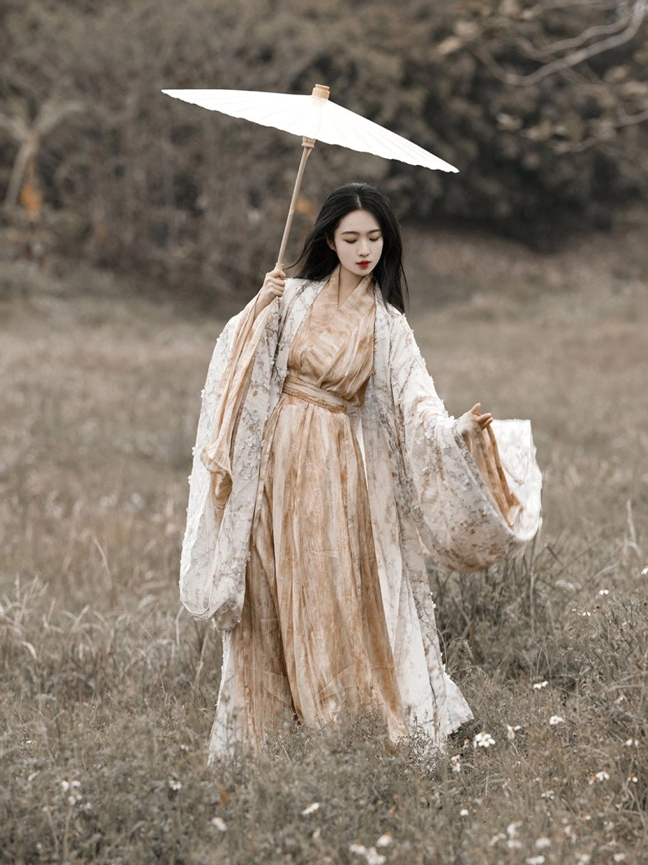 Full front view of a traditional Jin-style Hanfu set with a loose floral outer coat wide sleeves beige inner dress and orange waist sash outdoors