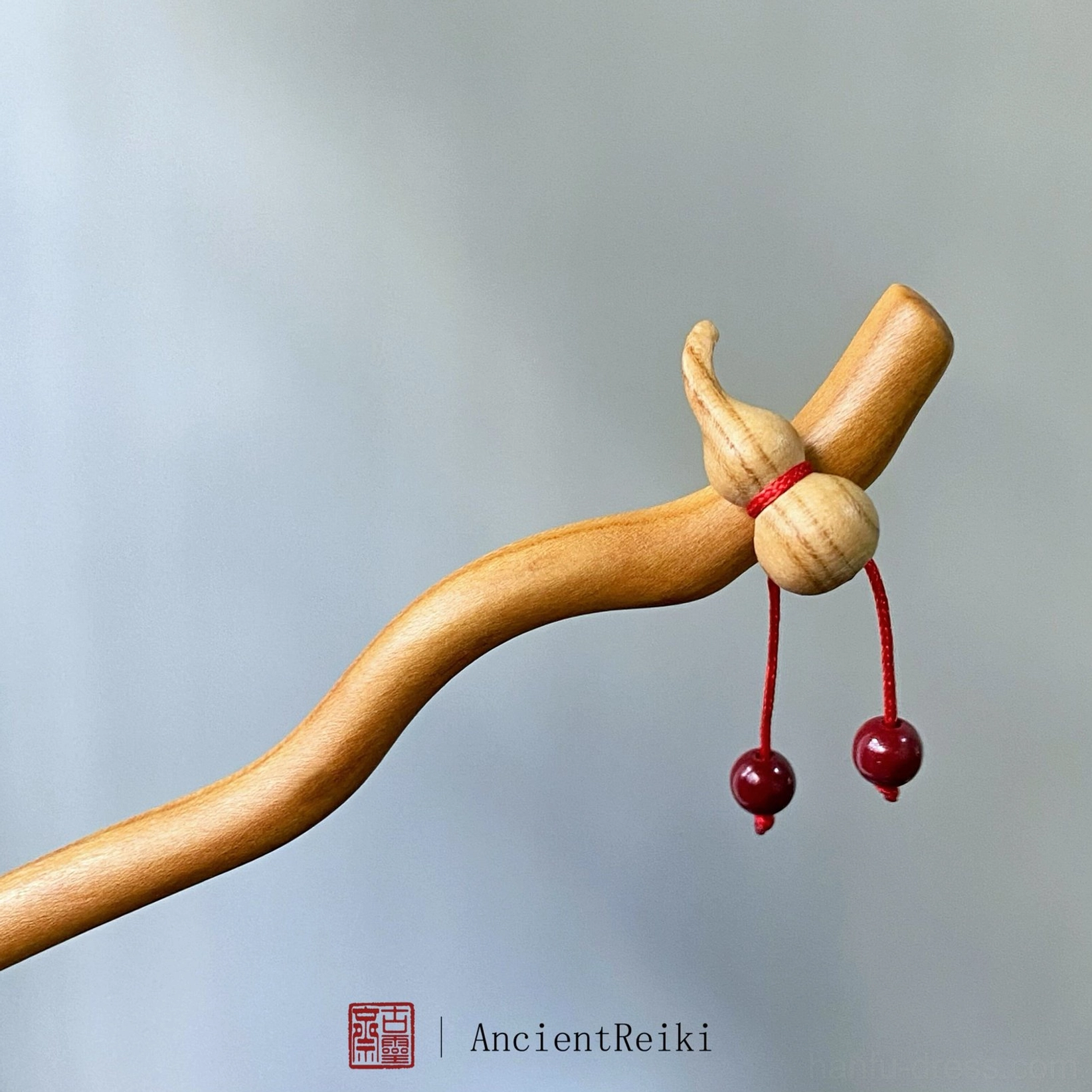 Angled view of traditional peach wood Chinese hair stick with hulu gourd decoration and red bead tassel details