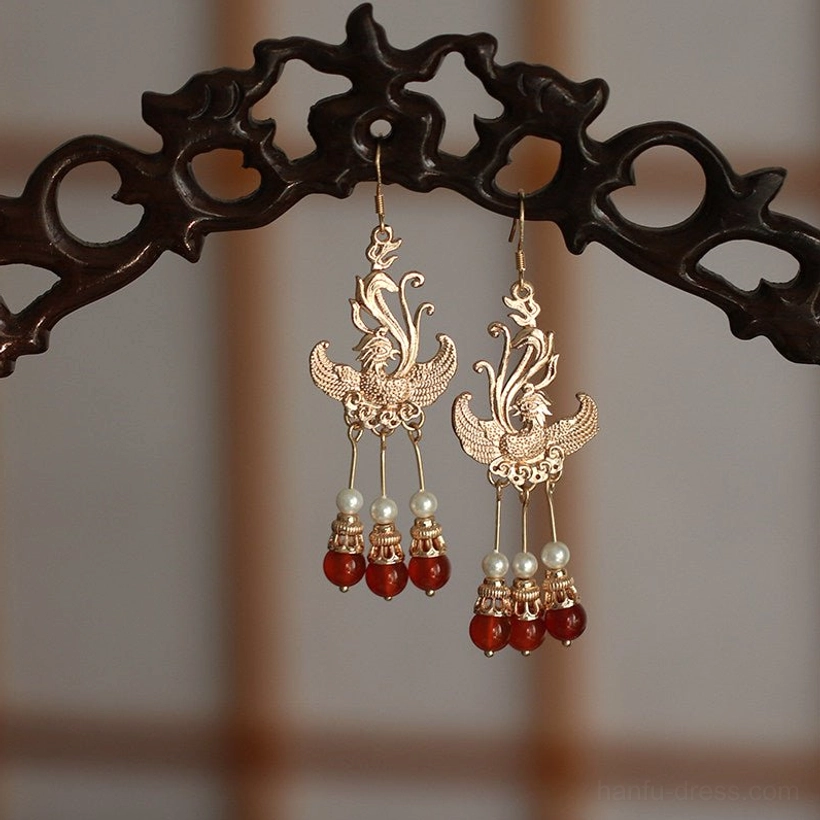 Traditional phoenix Chinese dangle earrings with retro gold motifs and subtly varied pearl and red bead tassel details on a carved wooden display