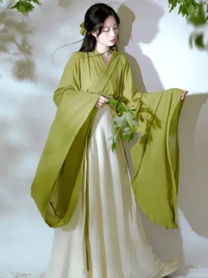 Three-quarter view of a traditional Wei Jin Dynasty Hanfu with olive green cross-collar top, wide flowing sleeves, ivory pleated skirt, and matching sash
