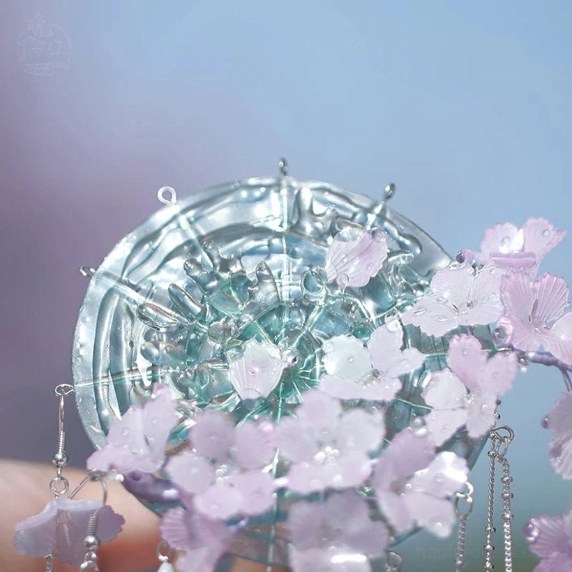 Close-up detail of the translucent cyan circular base on a Chinese hair stick with delicate flower petals and silver tassel attachment points
