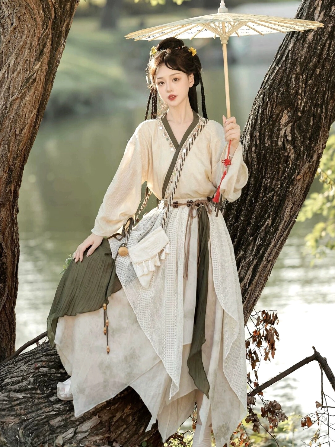 Seated model wearing Travelling Lotus modern Hanfu with loose long sleeves, textured layered skirt, and asymmetrical olive green hem