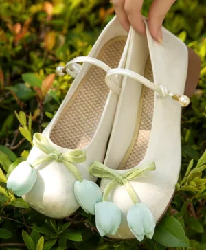 Close-up of traditional Chinese Hanfu shoes with light green tulip ornaments, pearl ankle strap, textured cream canvas upper, and low heel