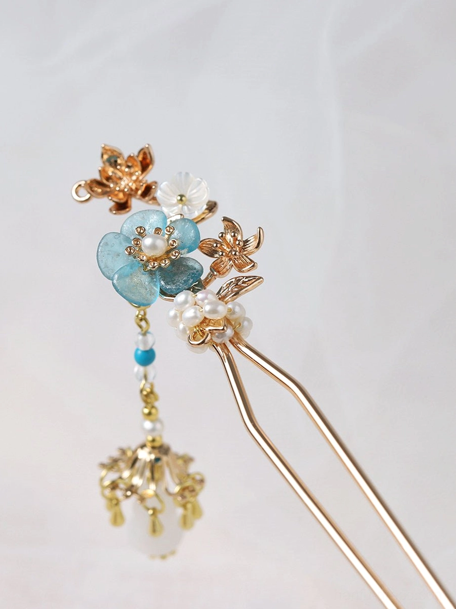 Close-up flat lay of turquoise blossom Chinese hair stick with golden floral details white petals pearl beads and bell-shaped tassel ornament