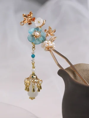 Turquoise blossom Chinese hair stick with white shell flowers pearl clusters gold-tone branches and dangling bead tassel displayed in a dark ceramic vase