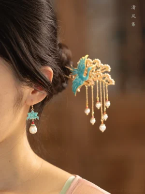 Female model wearing turquoise cloisonne lotus pearl Chinese earrings with a matching traditional crane tassel hairpin in a warm vintage setting