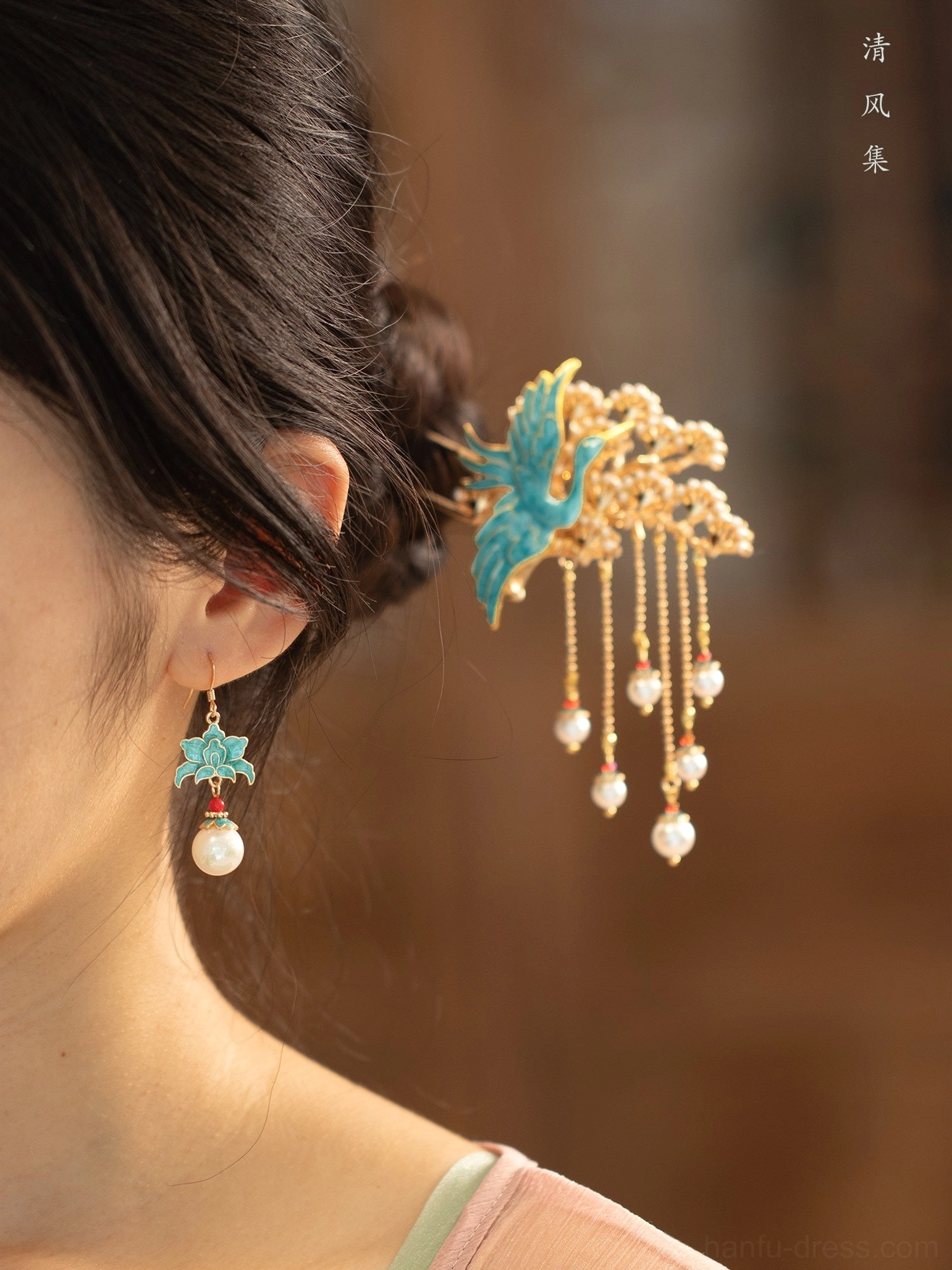 Female model wearing turquoise cloisonne lotus pearl Chinese earrings with a matching traditional crane tassel hairpin in a warm vintage setting