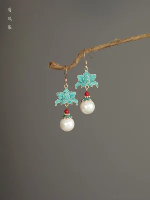 Turquoise cloisonne lotus drop Chinese earrings hanging from a natural twig, featuring a red accent bead, white pearl pendant, and gold toned hardware