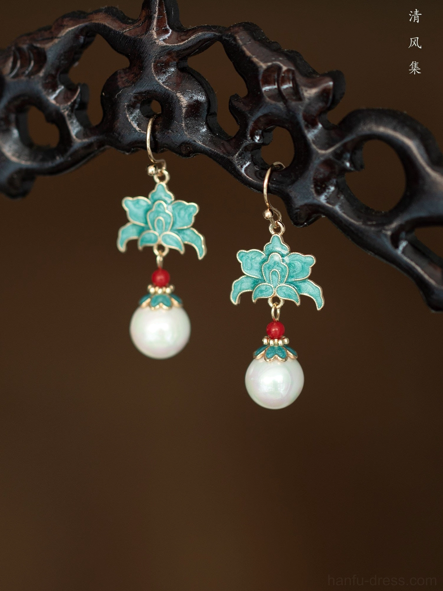 Front view of turquoise cloisonne lotus pearl drop earrings displayed on a dark carved wooden stand with gold hook findings