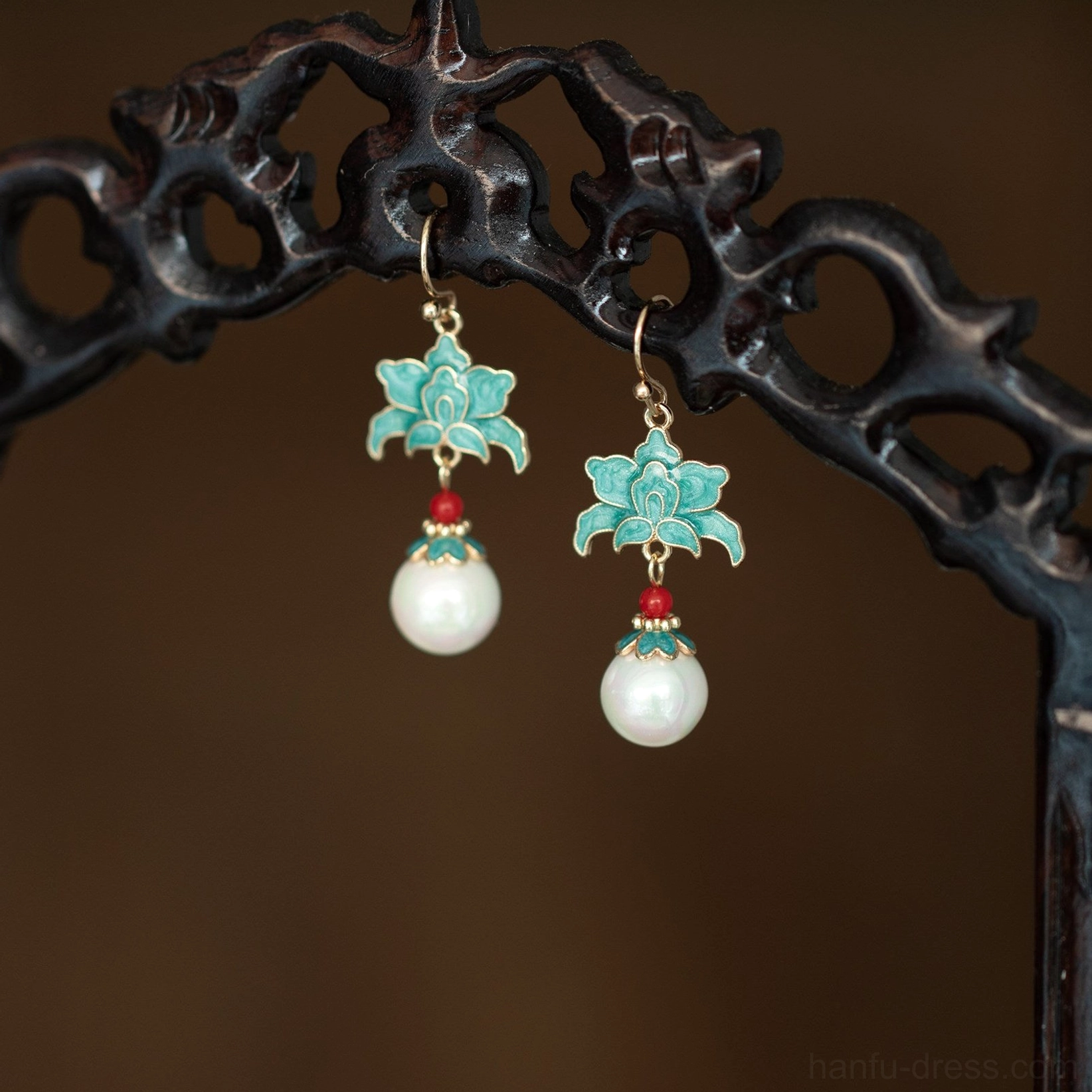 Turquoise cloisonne lotus pearl drop Chinese hook earrings displayed on a dark carved wooden stand with red bead accents