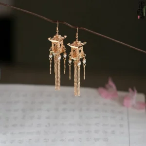 Twelve Midnight Palace antique Chinese Hanfu earrings with gold-toned palace pavilion filigree, pearl drops, and long chain tassels displayed on a branch