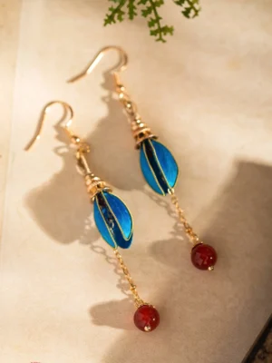 Blue flower bud dangle Chinese Hanfu earrings with gold hooks, gold-edged petals, red agate pendants, and delicate chains displayed on vintage rice paper