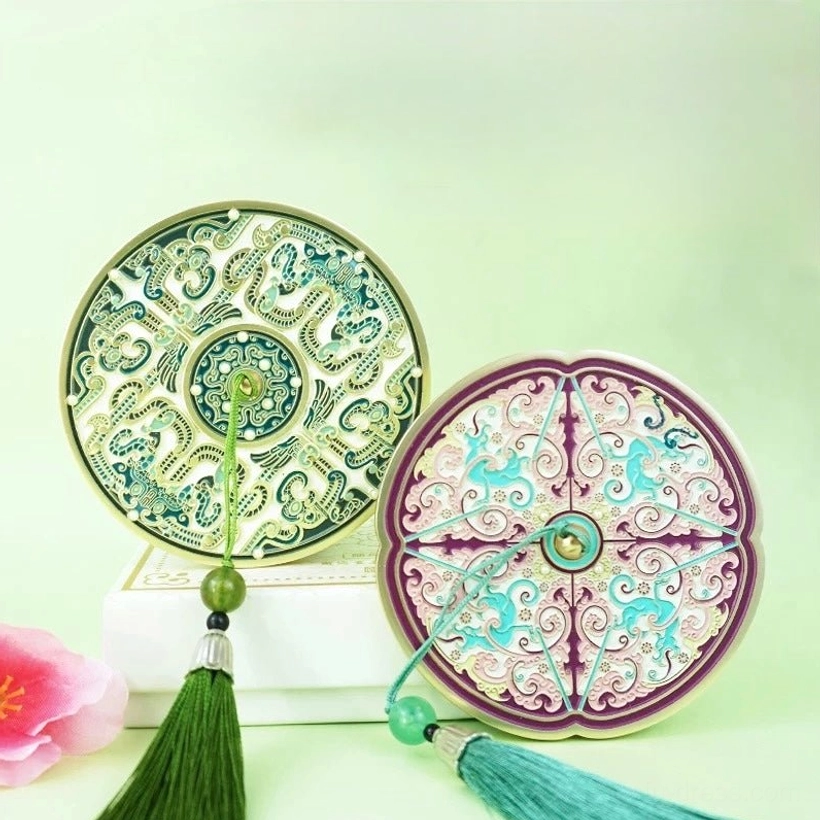 Two Chinese tassel pocket mirrors showing the Jade green round design and Amethyst purple quatrefoil design with colorful traditional ornamentation