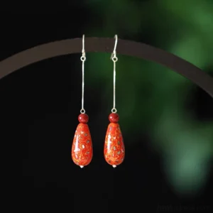Pair of vermilion lacquer teardrop Chinese drop earrings displayed on dark studio jewelry stand