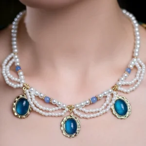 Close-up view of a vintage blue gem pearl Chinese necklace worn around the neck, featuring layered white pearl chains, light blue bead accents, and three deep blue oval pendants in ornate gold-tone frames