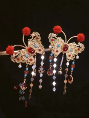 Pair of vintage butterfly hanfu hair pins with gilt filigree wings, red pom-poms, colorful gemstones, crystal beads, metal charms, and dangling tassels on a black background