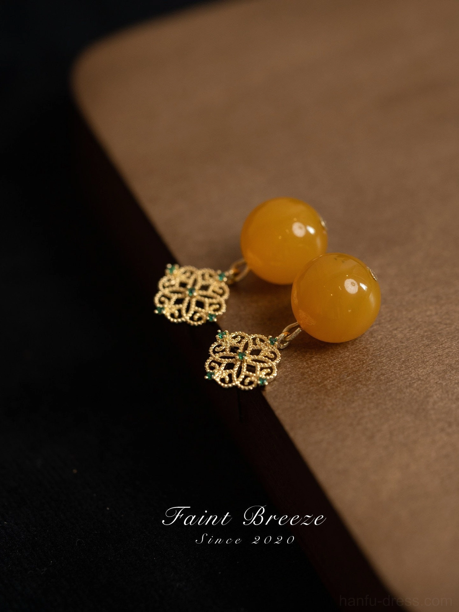 Pair of amber-colored dangle Chinese earrings with delicate gold filigree connectors and polished round pendants arranged on a brown vintage surface