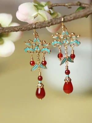 Pair of vintage Chinese cloisonne red agate drop earrings displayed on flowering tree branches in natural light