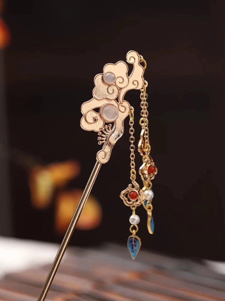 Oblique view of a vintage Chinese hair stick featuring a carved cloud design, pink decorative stones, red tassel accents, pearl details, and blue leaf pendants