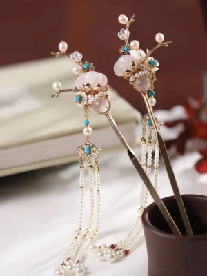 Oblique view of a pair of vintage Chinese hair sticks with gold branch details, milky white stones, blue accents, and long pearl tassel pendants