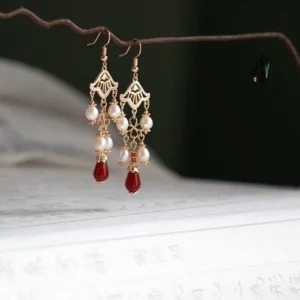 Side view of vintage Chinese Hanfu drop earrings featuring delicate gold filigree, linked pearl chains, and a red teardrop pendant on a dark green antique background