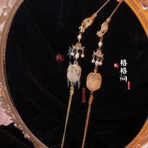 Pair of vintage Chinese lantern tassel hair pins with gold toned hollow lantern pendants pearl accents and long chain tassels displayed on a round mirror