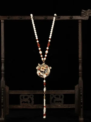 Vintage Chinese necklace with red agate beads white pearls gold floral pendant and long beaded tassel displayed on wooden jewelry stand
