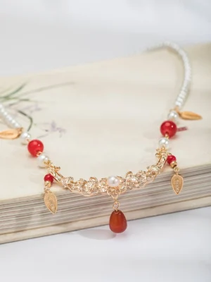 Chinese style pearl and red agate choker necklace flat lay on vintage painting book with gold floral filigree and leaf tassels