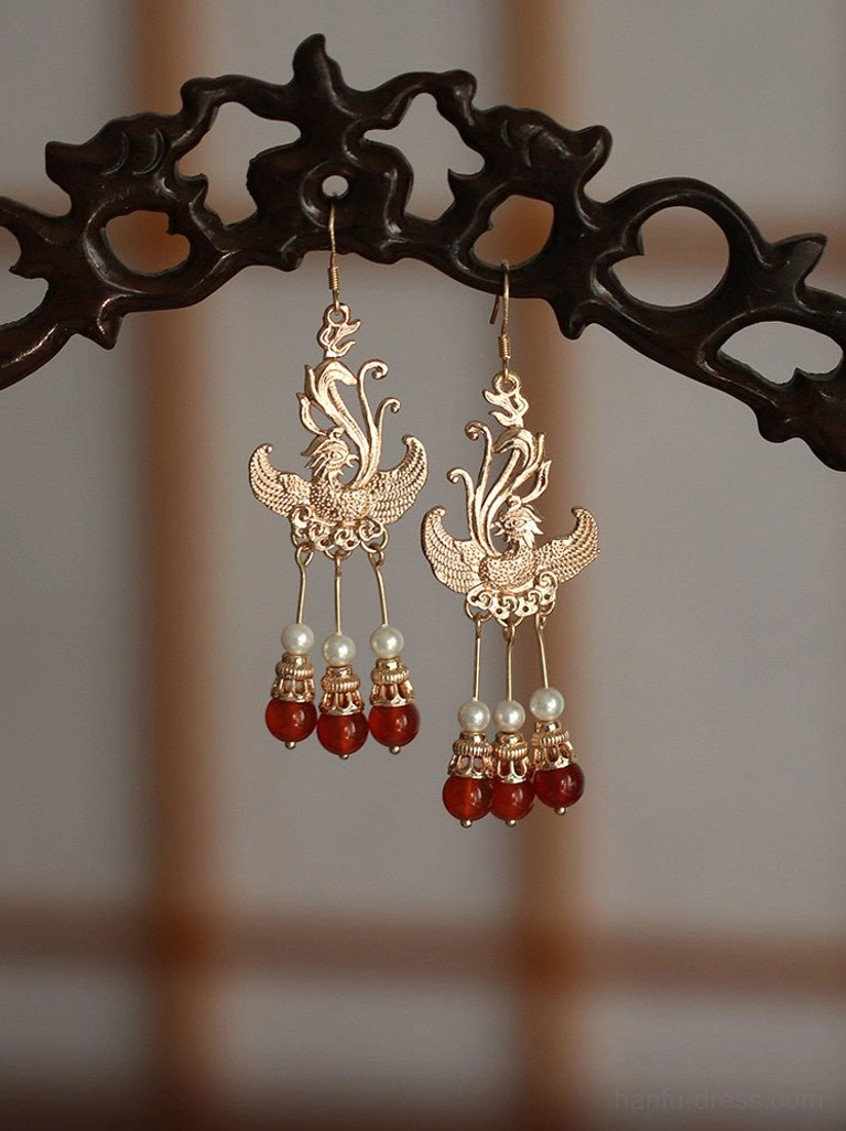 Vintage Chinese phoenix bridal earrings featuring hollow symmetrical phoenix patterns and a bright golden metallic finish on a wooden rack