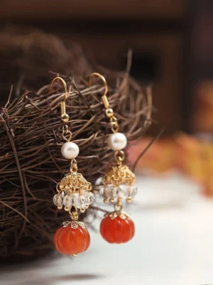 Vintage Chinese pumpkin drop earrings with glossy red pendants white pearls gold-toned hardware and sparkling crystal bead clusters displayed against a warm autumn backdrop