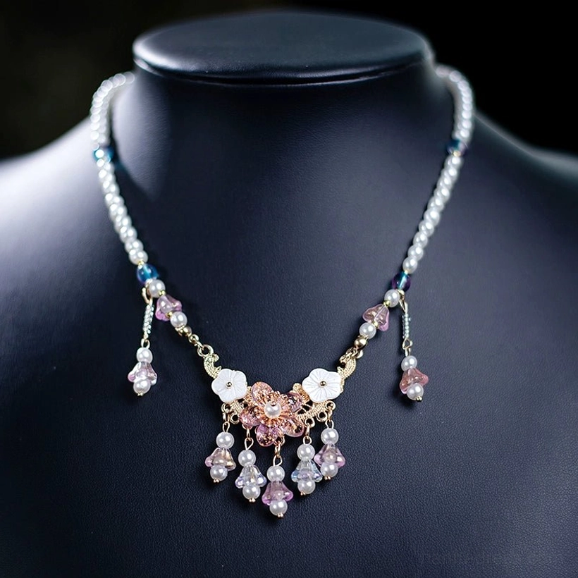 Front view of a vintage Chinese style tassel necklace displayed on a black mannequin, featuring imitation pearl chains, blue purple beads, white shell flowers, pink gold carved flower pendants, crystal accents, and elegant hanging tassels