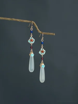Front view of vintage Chinese water drop Hanfu earrings hanging from a dry twig, featuring antique gold metalwork, cloud-shaped cloisonne-inspired ornaments, blue beads, deep red accents, and milky white pendants