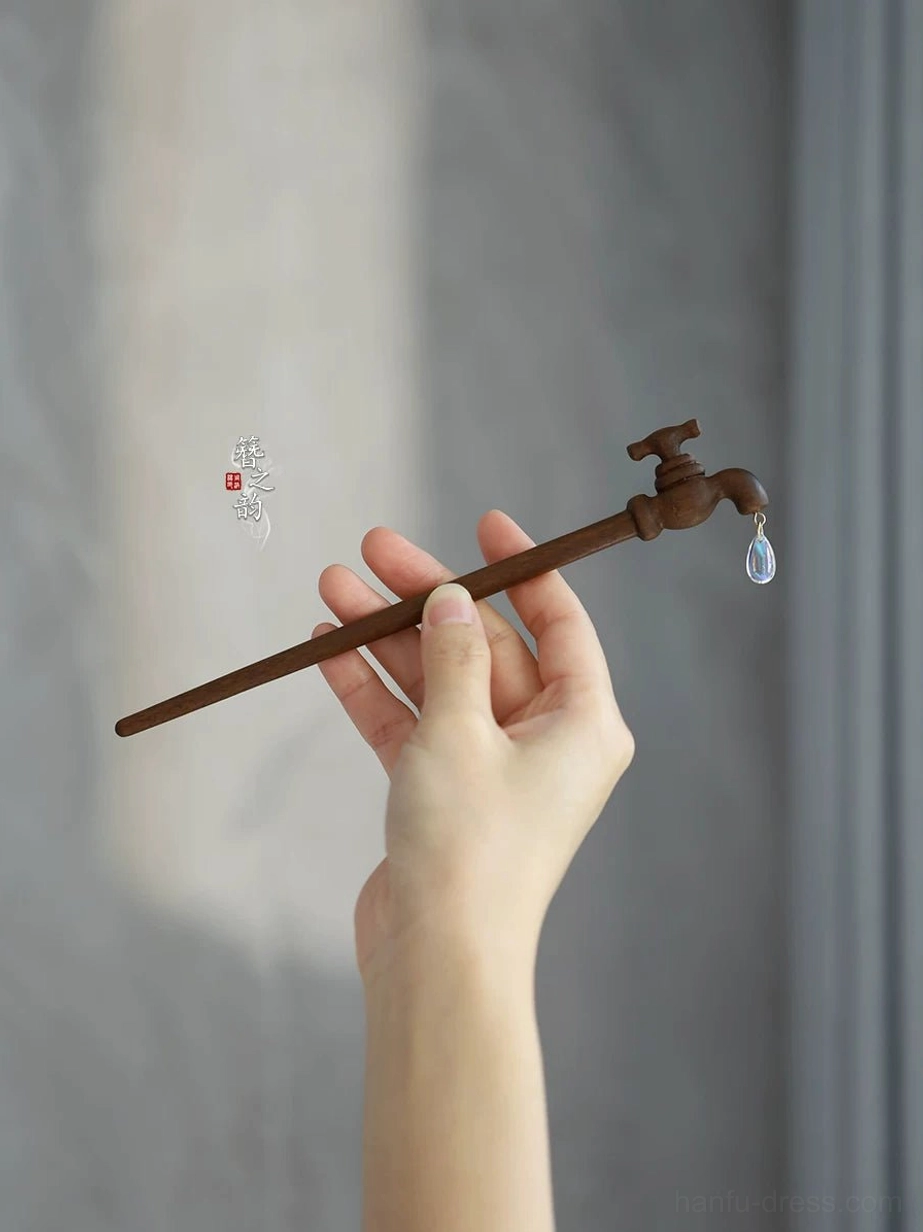Hand holding vintage faucet style dark brown wooden Chinese hair stick with sparkling clear teardrop pendant