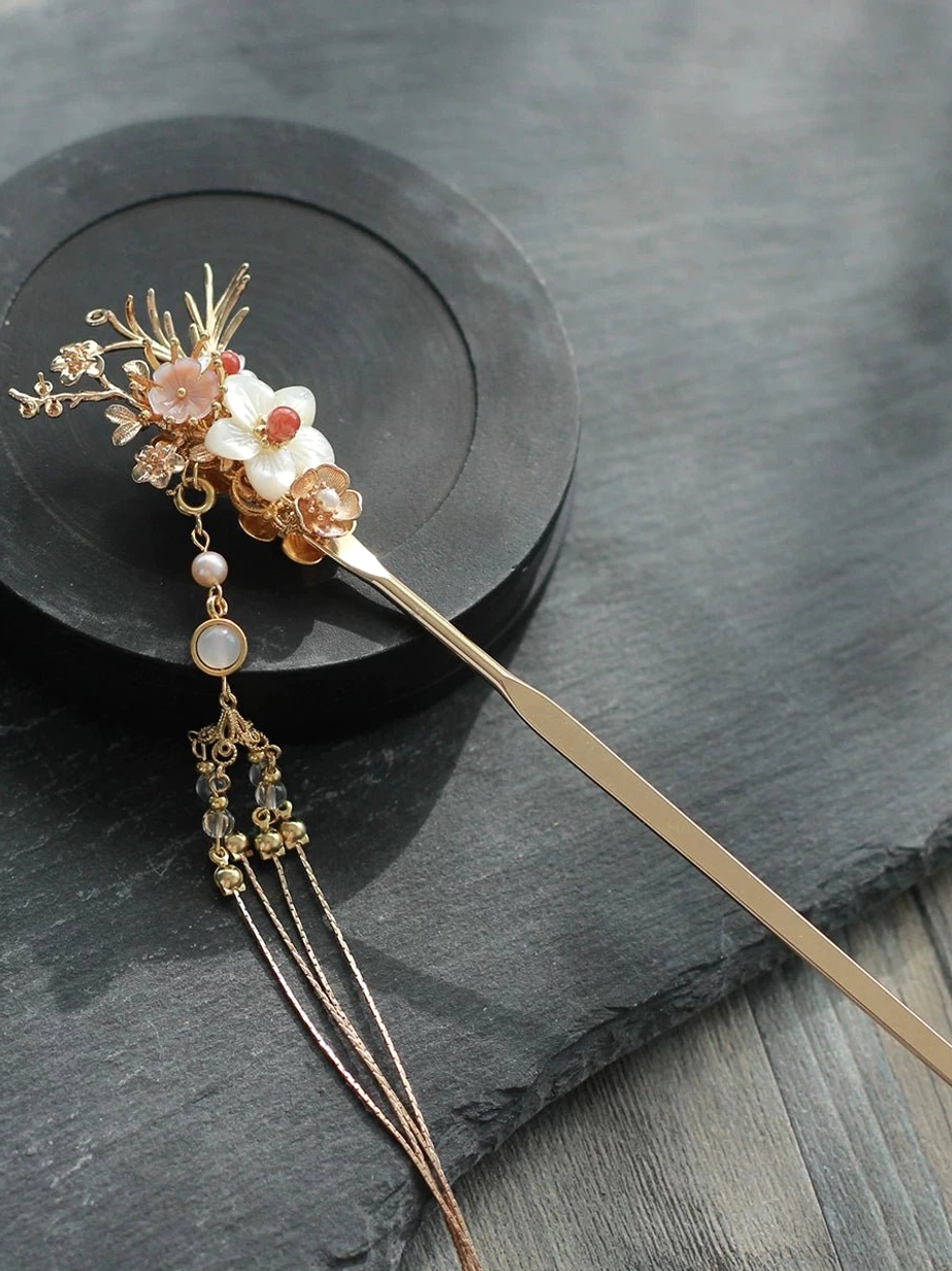 Vintage floral Chinese hair stick with rose gold metal finish, mixed flower decorations, pearl accents, and a decorative beaded tassel on a dark wooden surface