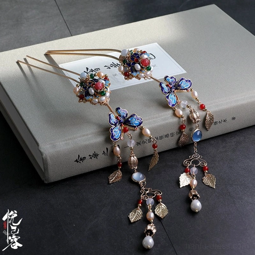 Chinese tassel hair pin with vintage gold frame, cloisonne butterfly, enamel flower, red beads, golden leaf charms, and pearl pendant displayed on a book