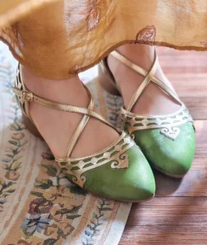 Model wearing vintage sage green and gold Mary Jane qipao heels with pointed toes, ornate cutout toe caps, crisscross ankle straps, and low block heels with a yellow embroidered Chinese dress