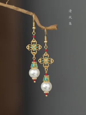 Vintage inspired Hanfu Chinese earrings with white pearl drops gold filigree charms turquoise enamel accents and red decorative beads angled close up
