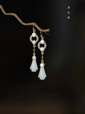 Vintage inspired magnolia Hanfu earrings with delicate gold filigree style accents white floral pendants and green bead details on dark brown background