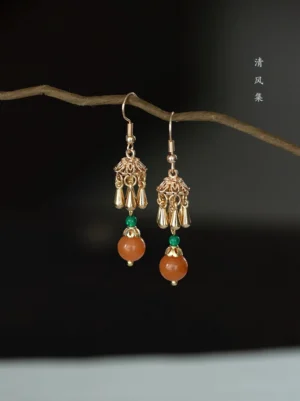 Vintage persimmon drop earrings for Hanfu jewelry displayed on a dry branch, featuring orange beads, green accent beads, gold filigree caps, and hook ear wires