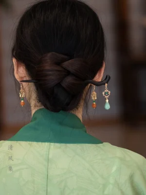 Woman wearing green Hanfu and a low bun with Chinese style drop earrings featuring orange persimmon-inspired beads and delicate gold-tone hardware