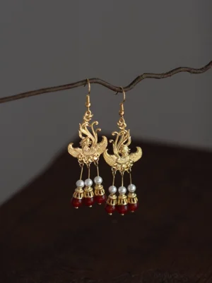 Vintage phoenix Hanfu dangle earrings with delicate phoenix ear hooks pearl drops and red bead tassels displayed against a dark wooden background