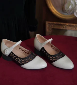 Vintage black and ivory Qipao Mary Jane heels with geometric cutout vamp, pointed toe, adjustable ankle buckle strap, and low block heel displayed on a burgundy velvet table