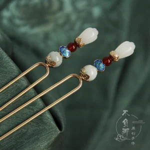 Vintage double-pronged Chinese hair stick featuring magnolia blossom details, jade beads, red agate accents, blue cloud ornament, and gold-tone metal shaft on dark green satin