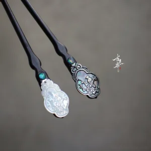 Traditional Chinese hair stick pair with dark wood shafts turquoise inlay and carved shell ornaments displayed beside Chinese calligraphy artwork