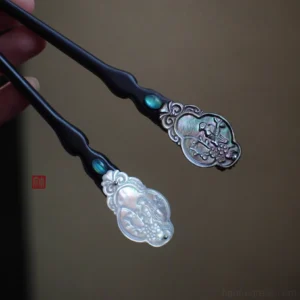 Close-up of black wooden Chinese hair sticks with turquoise-toned inlay and white and dark carved shell decorative heads held in hand