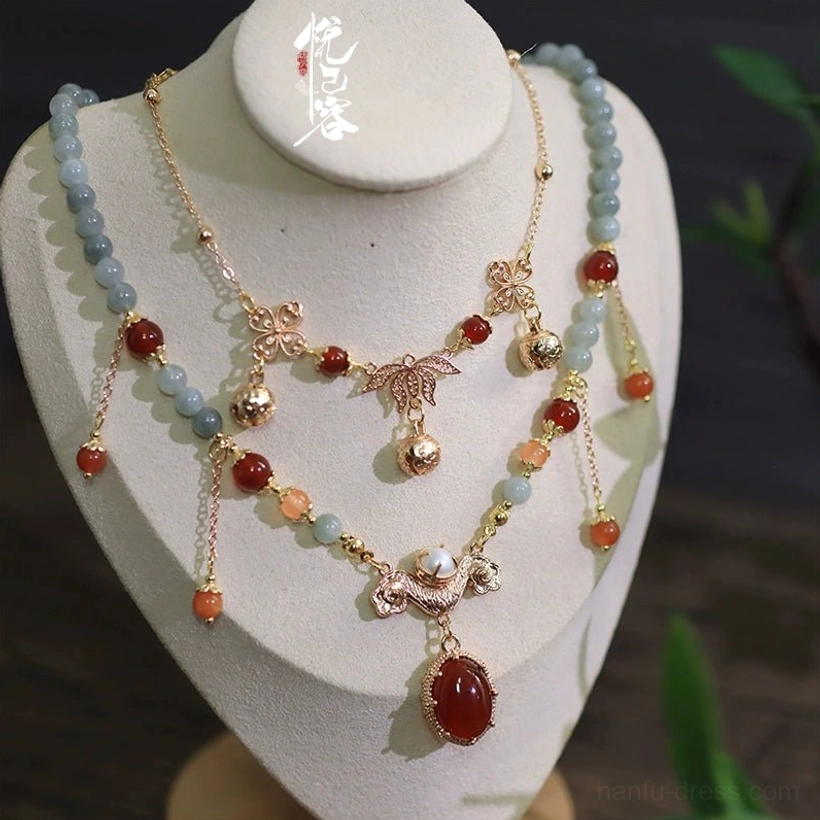 Double-layered vintage Chinese Hanfu necklace with gold-tone chains, light blue beads, red agate accents, oval warm wine red pendant, and dangling tassels displayed on a white jewelry mannequin